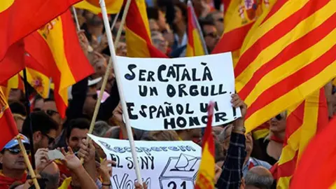 A protester holds a sign reading  Being Catalan is a pride  being Spanish is an honour  as others wave Spanish and Catalan Senyera flags during a pro-unity demonstration in Barcelona on October 29  2017  Pro-unity protesters were to gather in Catalonia s capital Barcelona  two days after lawmakers voted to split the wealthy region from Spain  plunging the country into an unprecedented political crisis    AFP PHOTO   LLUIS GENE